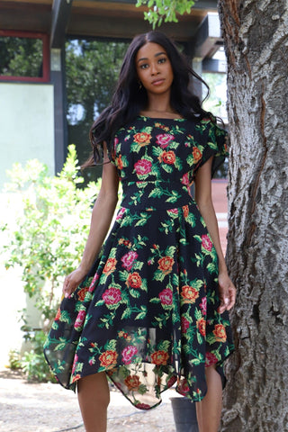 a woman standing next to a tree wearing a black floral dress