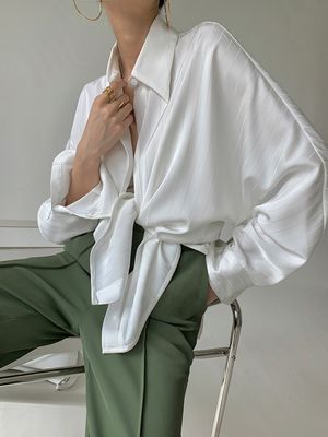 a woman sitting on a chair wearing a white shirt and green pants