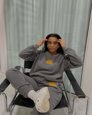 a woman sitting in a chair wearing a grey sweatshirt and white sneakers