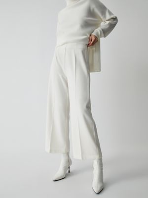 a woman wearing a white sweater and wide pants