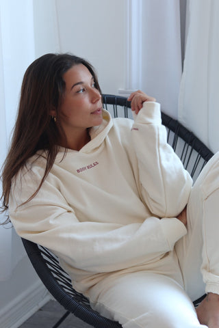 a woman sitting in a chair wearing a white sweatshirt and white pants