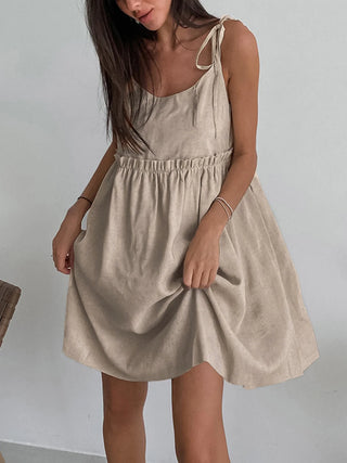 a woman in a beige dress standing next to a chair