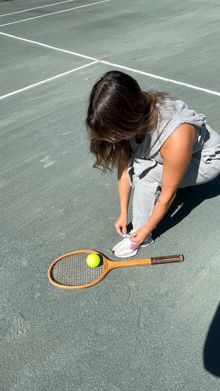 a woman crouching down to pick a tennis ball