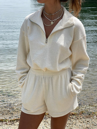 a woman wearing a white sweater and shorts by the water