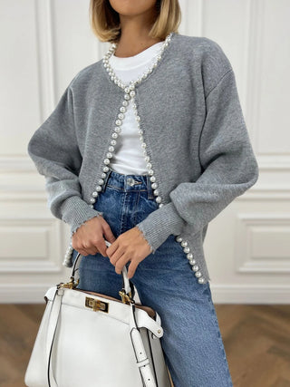 a woman wearing a grey sweater with pearls and a white bag