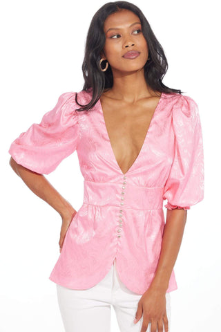 a woman wearing a pink top with a plunging neck and puff sleeves