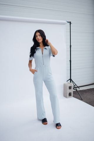 a woman standing in front of a white backdrop wearing a blue jumpsuit