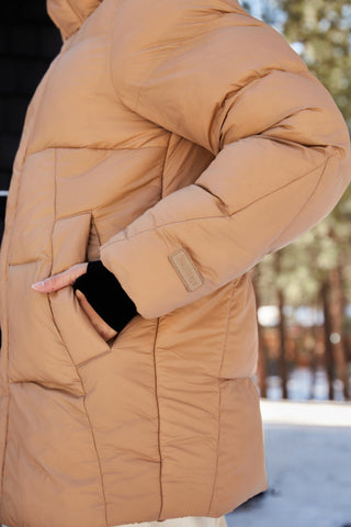 a woman in a brown parka and white pants