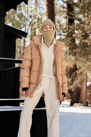 a woman standing in the snow wearing a beige jacket and white pants