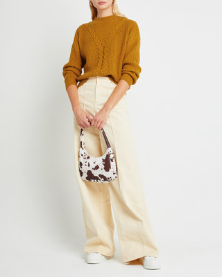 a woman in a mustard sweater and cream pants holding a brown and white bag