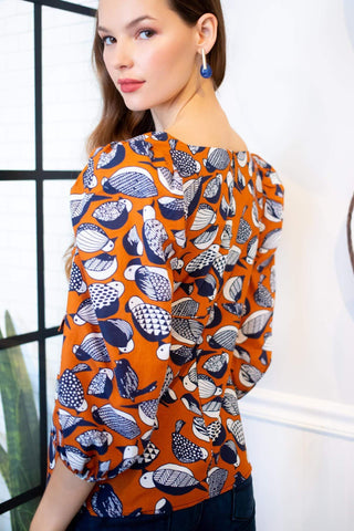 a woman wearing an orange top with blue and white fish print